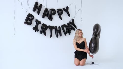 Attractive blonde lady in black dress sits on her knees in studio.