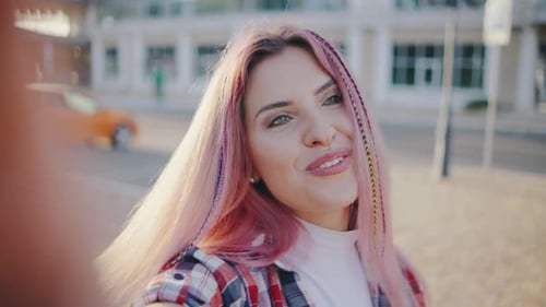 Beautiful Young Hipster Woman with Pink Hair Takes a Selfie in the Park or on the Street at Sunset