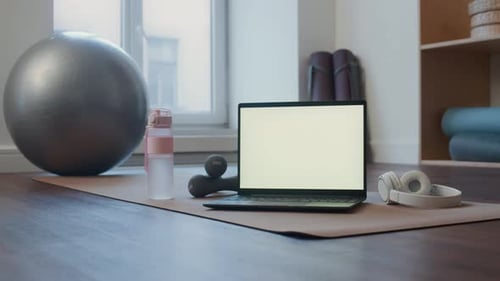 Laptop with Blank Screen and Fitness Equipment on Floor in Home Gym