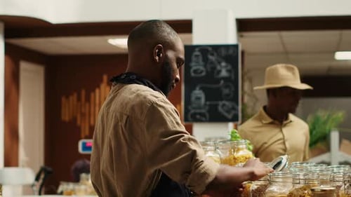 Merchant with Apron Placing Bulk Items on Shelves at Eco Store