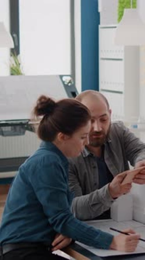 Vertical Video Colleagues Using Smartphone to Analyze Building Model and Blueprints Plan on Table