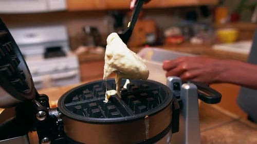 Young man making waffles for the family - spoons batter on the waffle iron in slow motion