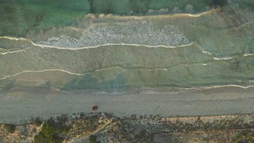 A top-down aerial view of a tranquil beach shows rhythmic waves rolling onto a sandy shore.