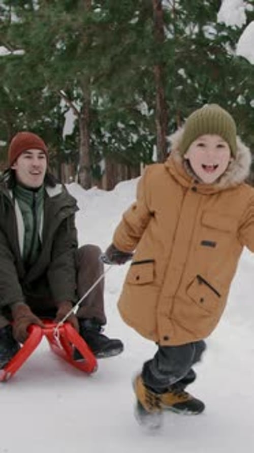 Niño birracial riendo dando un paseo en trineo en la nieve a su padre asiático