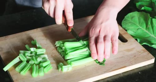 Chef chopping fresh, raw, green celery on chopping board, in the kitchen. Close up.