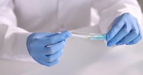 Scientifique tenant une bandelette de test de pH et un tube en verre avec un liquide à une table blanche en laboratoire, gros plan