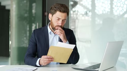 Man in Suit Looks at Documents at Desk