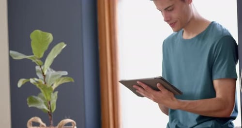 Young Man Using Tablet at Home by Window