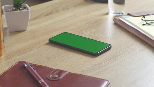 Close up of a mock up green screen smartphone on a desk at the office