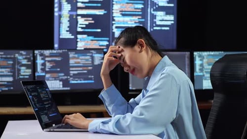 Vista lateral de una programadora asiática que tiene dolor de cabeza mientras escribe código con una computadora portátil