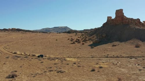 Aerial follows car through rocky desert landscape on rugged dirt road
