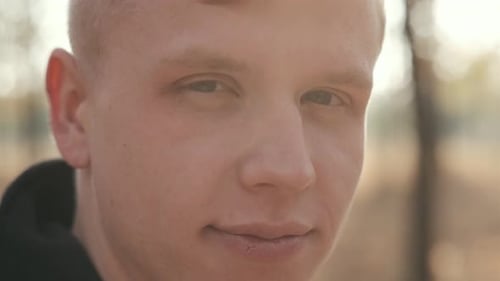 Portrait d'un bel homme en manteau noir assis près de l'arbre dans la forêt d'automne par une journée ensoleillée