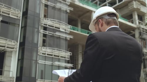 Engineer in a Suit and White Safety Helmet Standing with Blueprint at Construction Site Professional