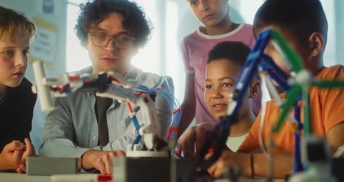 Team of Talented Kids Sitting at Table in Classroom Studying Robotic Arm Model with Teacher