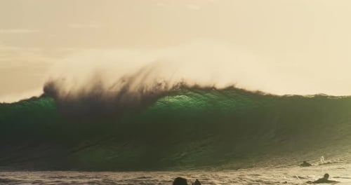 Surfers quickly paddle to get out of impact zone of huge glistening wave