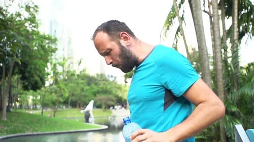 Young Male Jogger Drinking Water After Workout in City Park, Super Slow