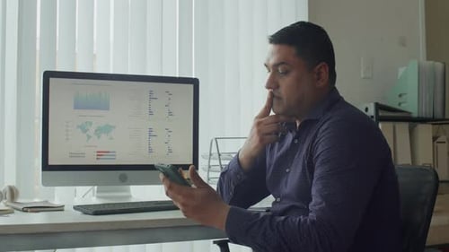 Employee Checking Report on Computer Using Smartphone at Office