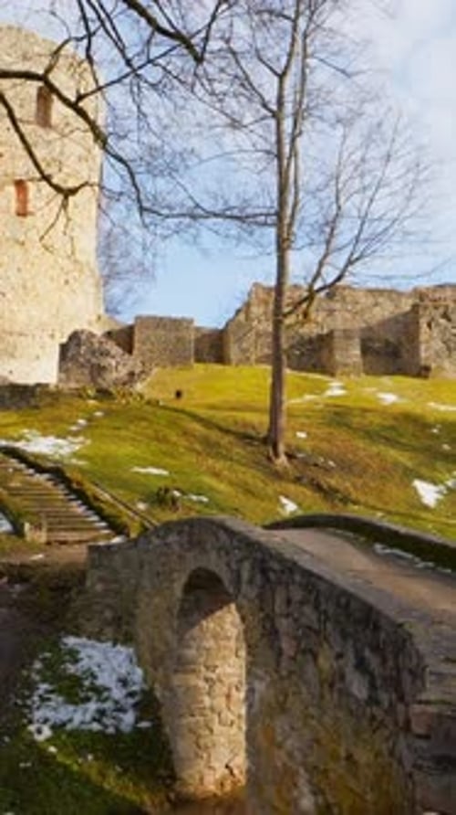 Vertical shot of a medieval stone fortress with round tower, ruins, and small arched bridge on a