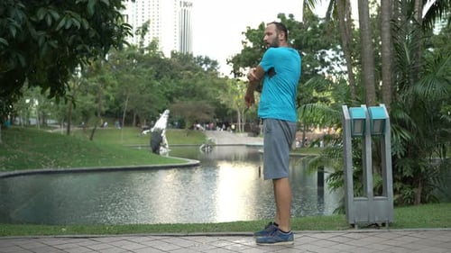 Young caucasian man stretches arms warming up before run in city park