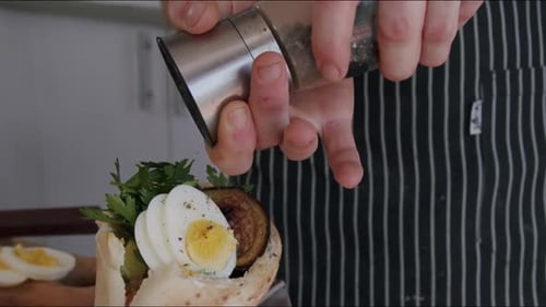 Chef Sprinkling Pepper on Pita Sandwich in Kitchen