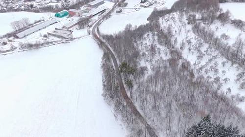 Ein Auto fährt durch eine winterliche Waldstraße, von oben gesehen, mit schneebedeckter Landschaft und Natur
