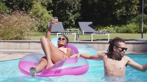 African American couple in suits, woman raising glass urging man holding float placing cup on towel