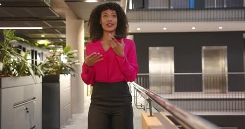 Walking through office, businesswoman using smartphone for voice message, smiling