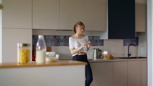 Woman Drinks Water After Workout in Modern Kitchen