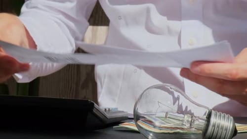 Electric Light Bulb Man Hands Counting Expenses Bills on Electricity Banknotes of Euro Cash