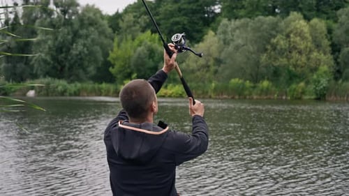 Fisherman with fishing rod or spinning and professional tools sitting on the river bank rear view