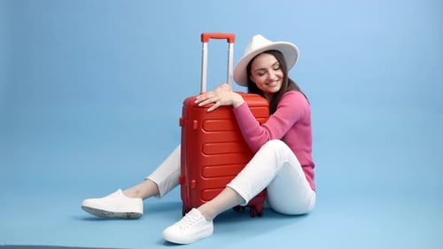 Happy young tourist woman sitting at the suitcase, hugging it and going to travel on holidays