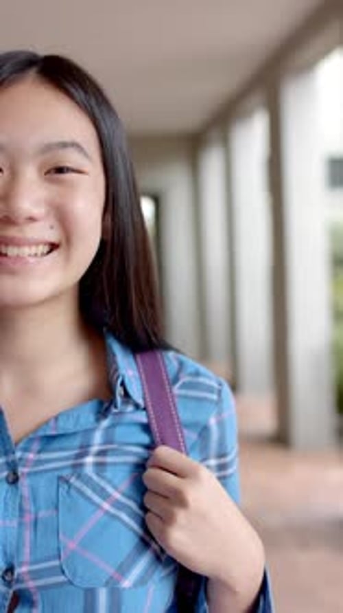 Vídeo vertical: En la escuela secundaria, una joven estudiante asiática está sonriendo