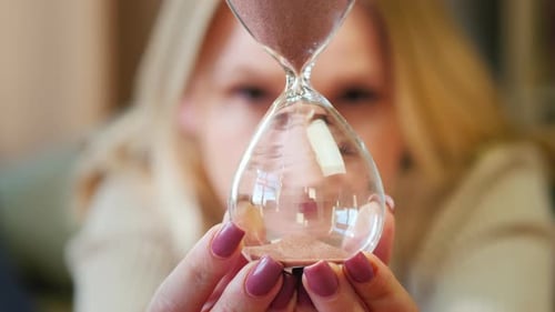 A Woman Looks at the Hourglass Where the Grains of Sand Fall Through Narrow Neck