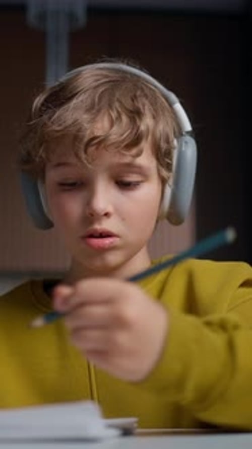 Young Boy with Curly Hair Wearing Large Overear Headphones and a Yellow Sweatshirt Focusing Intently