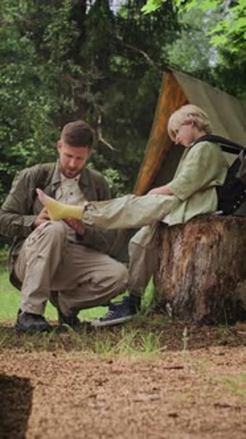 Father Taping Sons Strained Ankle during Family Camping Trip in Forest