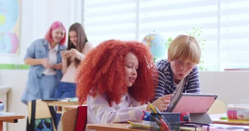 Porträt eines kleinen süßen kaukasischen Schulmädchens und eines Schuljungen, die am Schreibtisch im Klassenzimmer mit Tablet sitzen