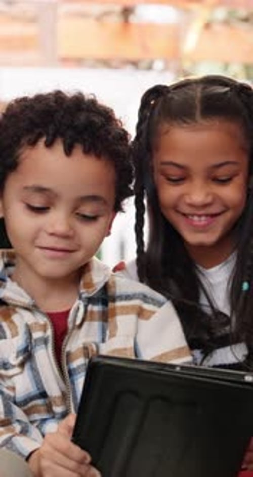 Happy Kids Sharing a Tablet Indoors During the Day