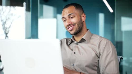 Cheerful businessman employee communicates online via video call while sitting in office at workplac