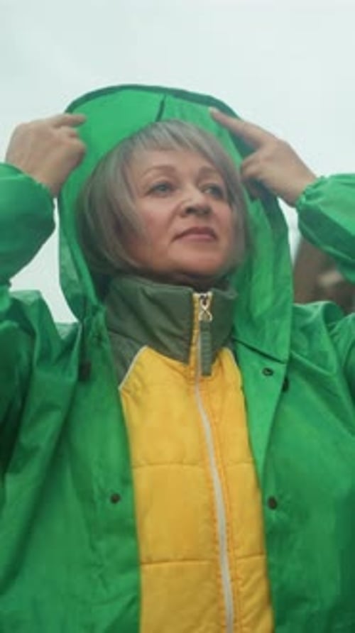 Middleaged Woman Adjusts Green Raincoat Hood Near Swing Bench in Outdoor Setting