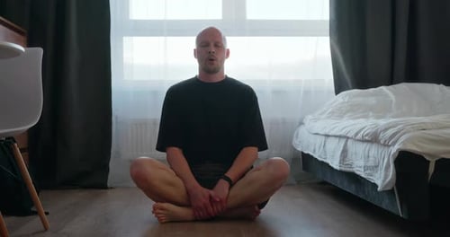 A Man is Doing Breathing Exercises Sitting on the Bedroom Floor
