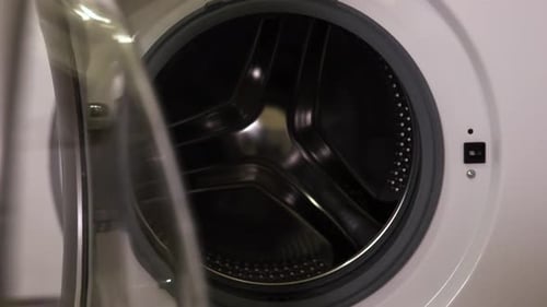 Um homem joga roupas na máquina de lavar no quarto