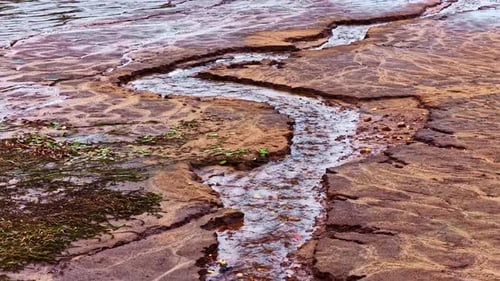 Dry cracked earth with water stream, drought impact, aerial view
