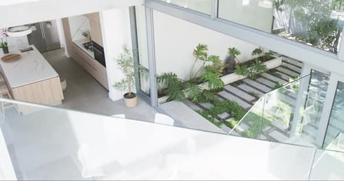 A modern kitchen with marble countertops overlooks a small garden with lush greenery