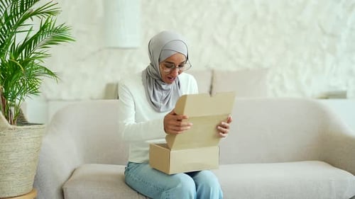 Young Muslim woman in hijab received a parcel satisfied with shopping in online internet store sit