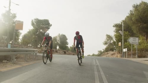 slow motion of two road cycelist professionals riding in the forest's empty road.