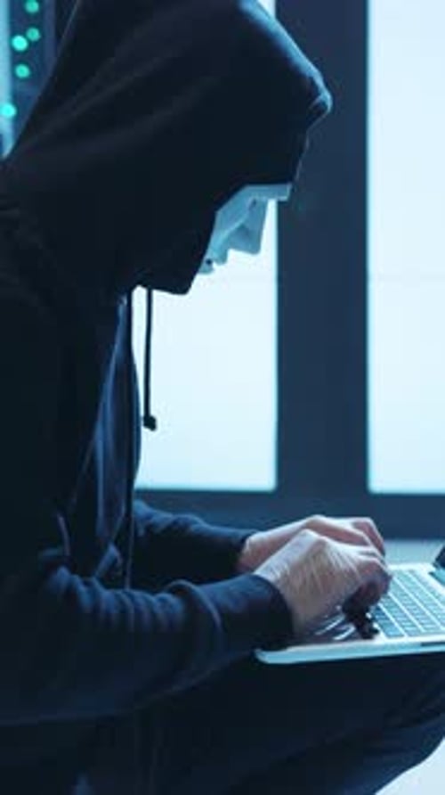 Hooded Figure Working on Laptop in Server Room