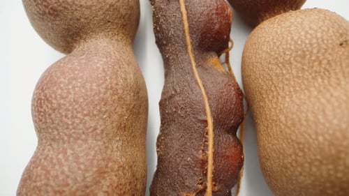 eine geschälte Tamarindenfrucht zwischen zwei ungeschälten Tamarindenfrüchten auf weißem Hintergrund. Dolly Slider extrem nah