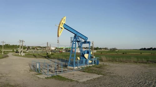 Industrieller Ölpumpenheber arbeitet auf freiem Feld unter blauem Himmel
