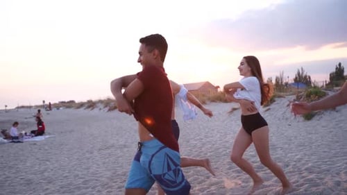 Group of Happy Friends Undress Running Into the Sea Water and Throw Shirts on the Beach Cheerful