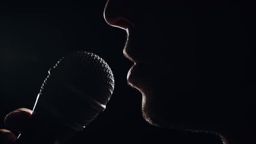 Person Speaking into Microphone Close-Up in Dramatic Silhouette